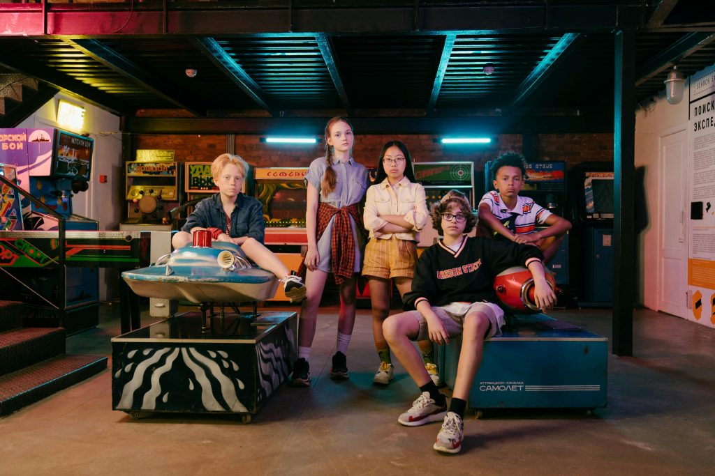 Teenagers posing confidently in a retro arcade, surrounded by neon lights and vintage games.