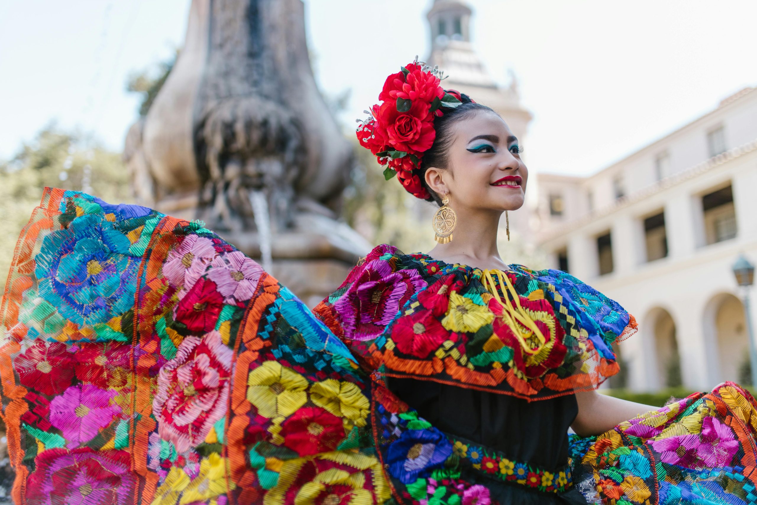 Woman in vibrant traditional Mexican attire with a flower crown, celebrating cultural heritage outdoors.